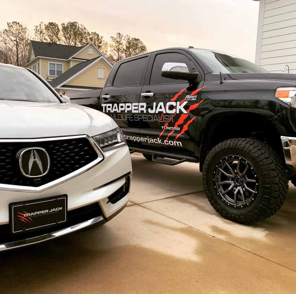 Two parked vehicles, an Acura and a black truck with 'Trapper Jack' decal.